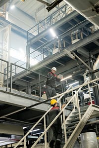 Foreman with tablet bending over staircase where female worker moving upwards