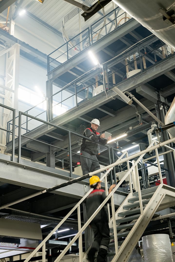 Foreman with tablet bending over staircase where female worker moving upwards